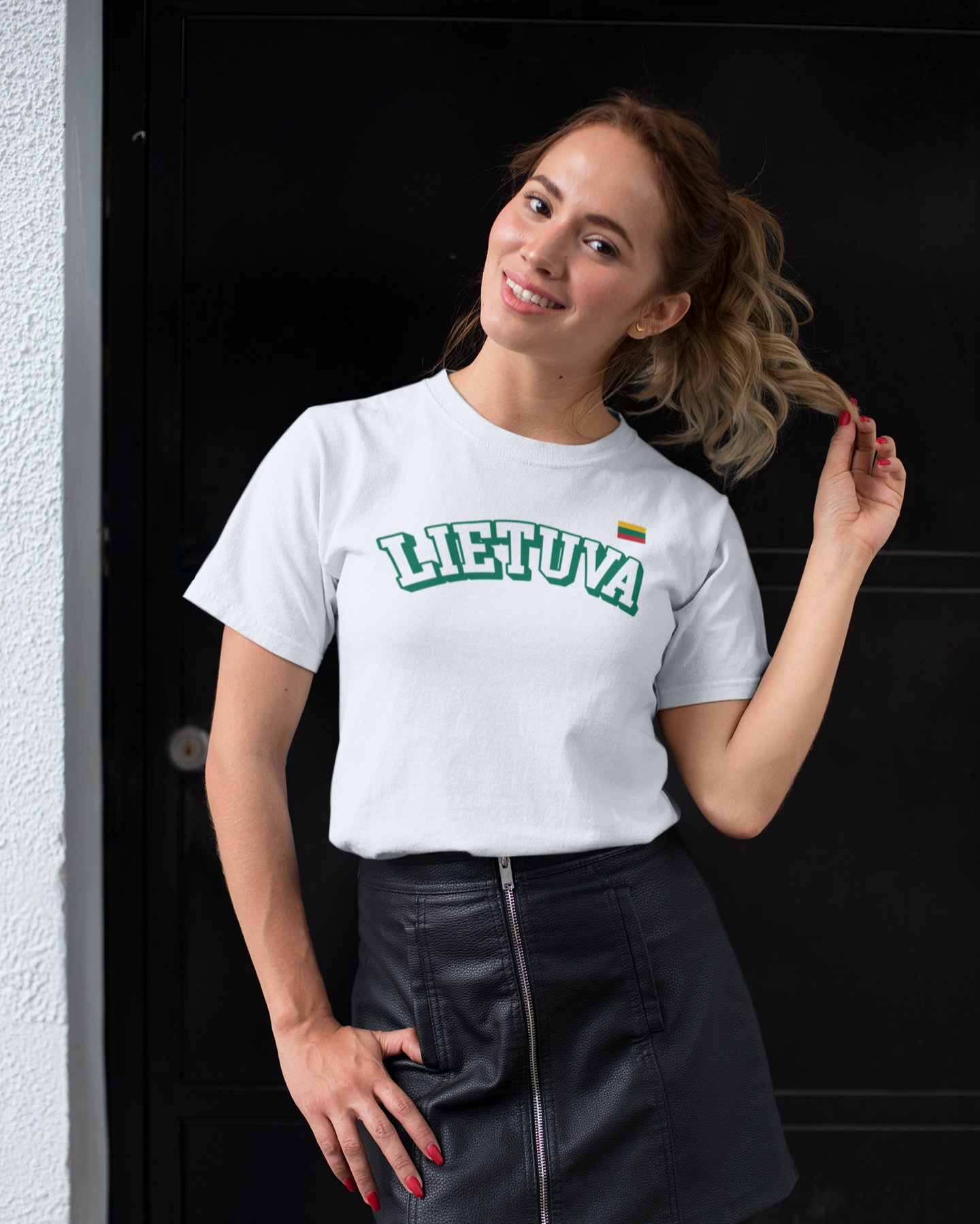 Besišypsanti moteris vilki lietuviško atributikos baltus marškinėlius su užrašu „LIETUVA“ ir trispalve vėliavėle