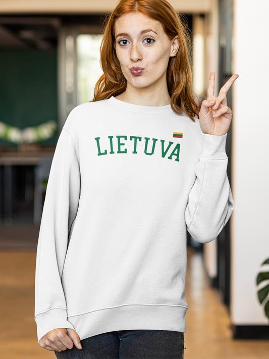 Patalpoje stovinti jauna moteris, rodanti taikos gestą, apsirengusi baltu džemperiu su užrašu „LIETUVA“ ir maža trispalve