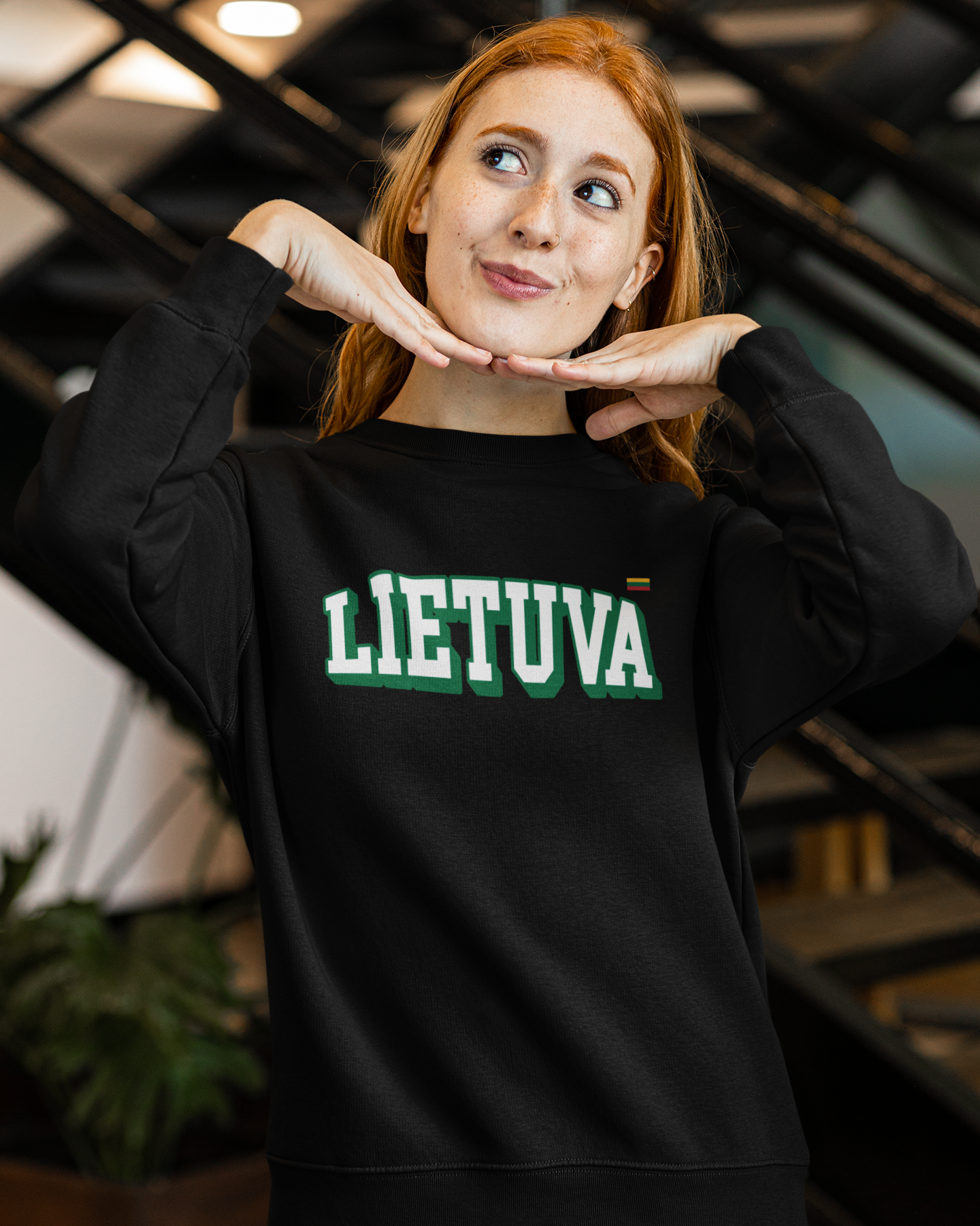 Moteris pozuoja vilkėdama juodą lietuviškos atributikos džemperį su užrašu „LIETUVA“ ir Lietuvos vėliavėle širdies srityje