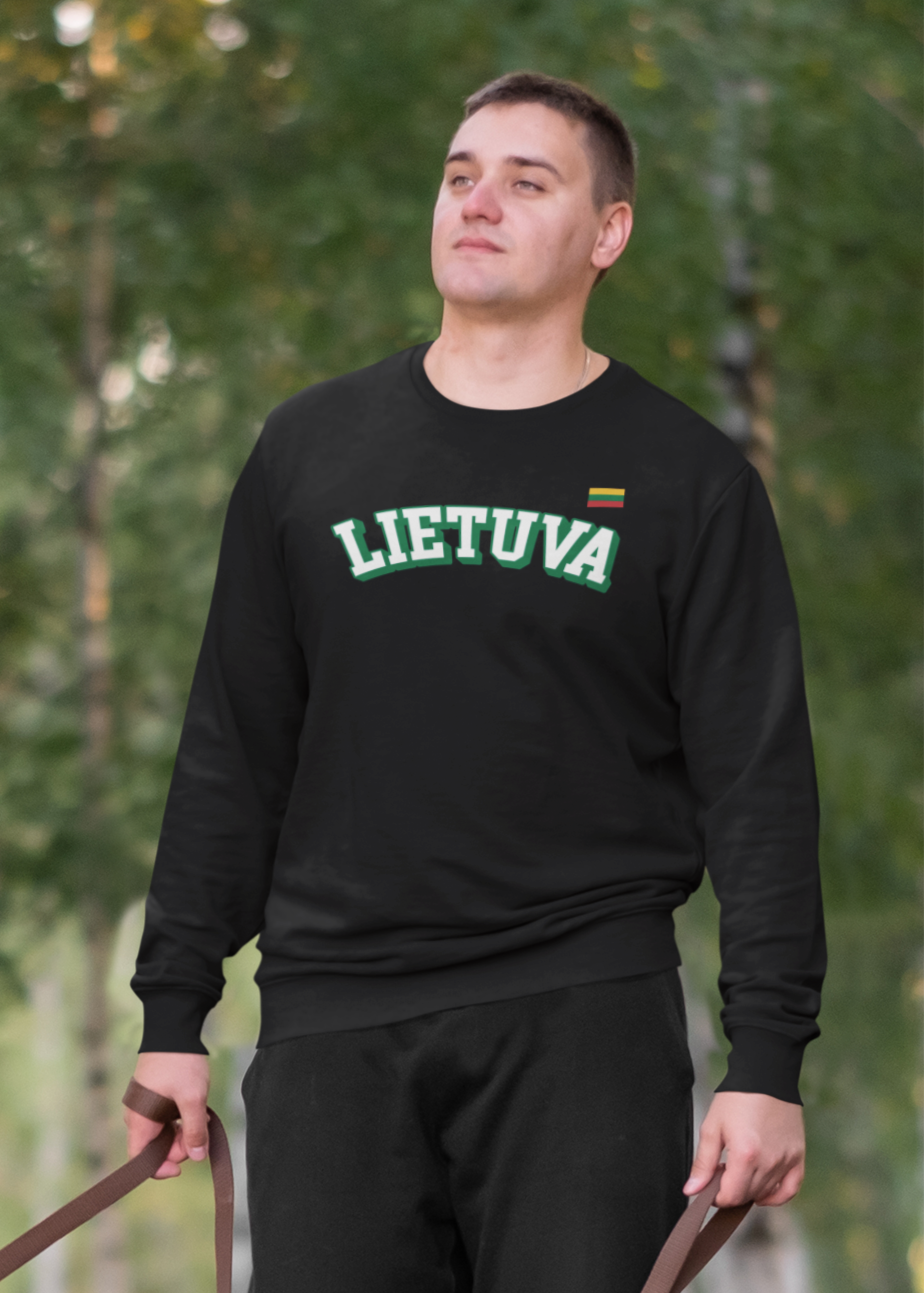 Vyras vedžiojantis parke šunį, vilkintis juodą džemperį su žaliu kontūruotu užrašu „LIETUVA“ ir Lietuvos trispalve vėliavėle