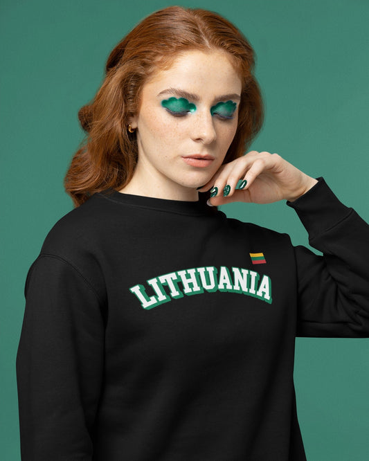 Rausvaplaukė moteris su ryškiu žaliu makiažu dėvi juodą džemperį su užrašu „LITHUANIA“ ir Lietuvos trispalve širdies plote