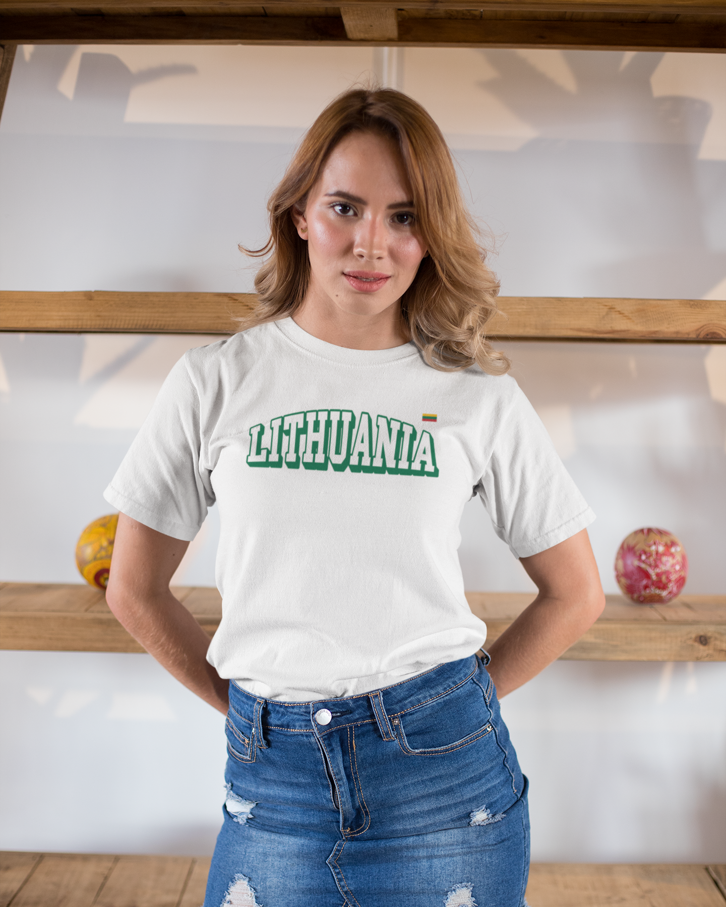 Moteris dėvinti baltus marškinėlius su užrašu "Lithuania" ir Lietuvos vėliavėle, stovi prie medinių lentynų.