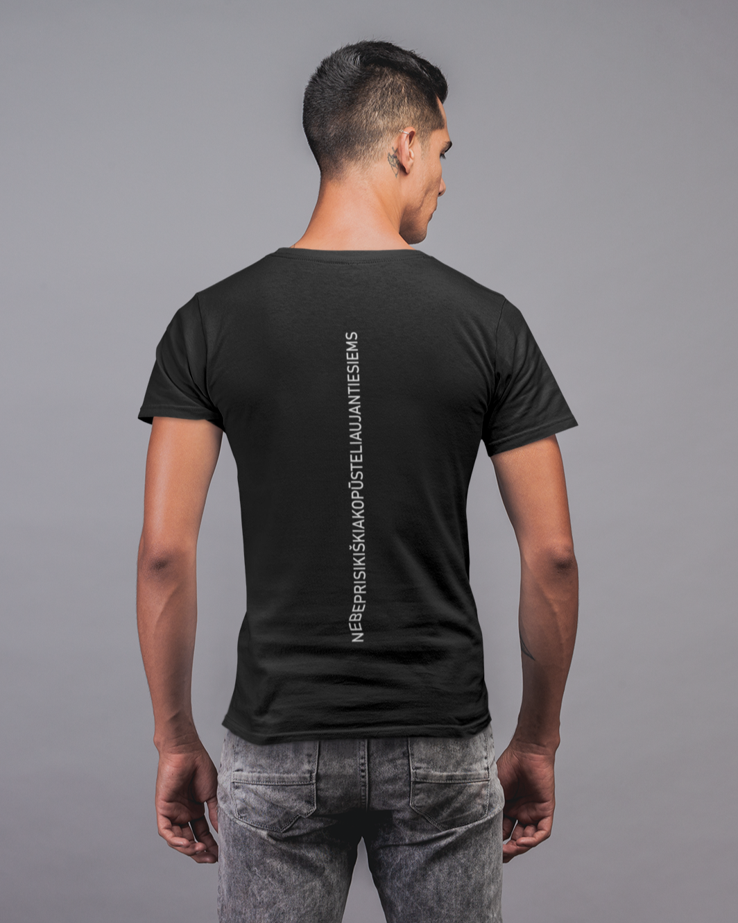 Vaikinas, nufotografuotas iš nugaros, dėvi juodus marškinėlius su ilgiausiu lietuvišku žodžiu užrašytu vertikaliai nugaroje