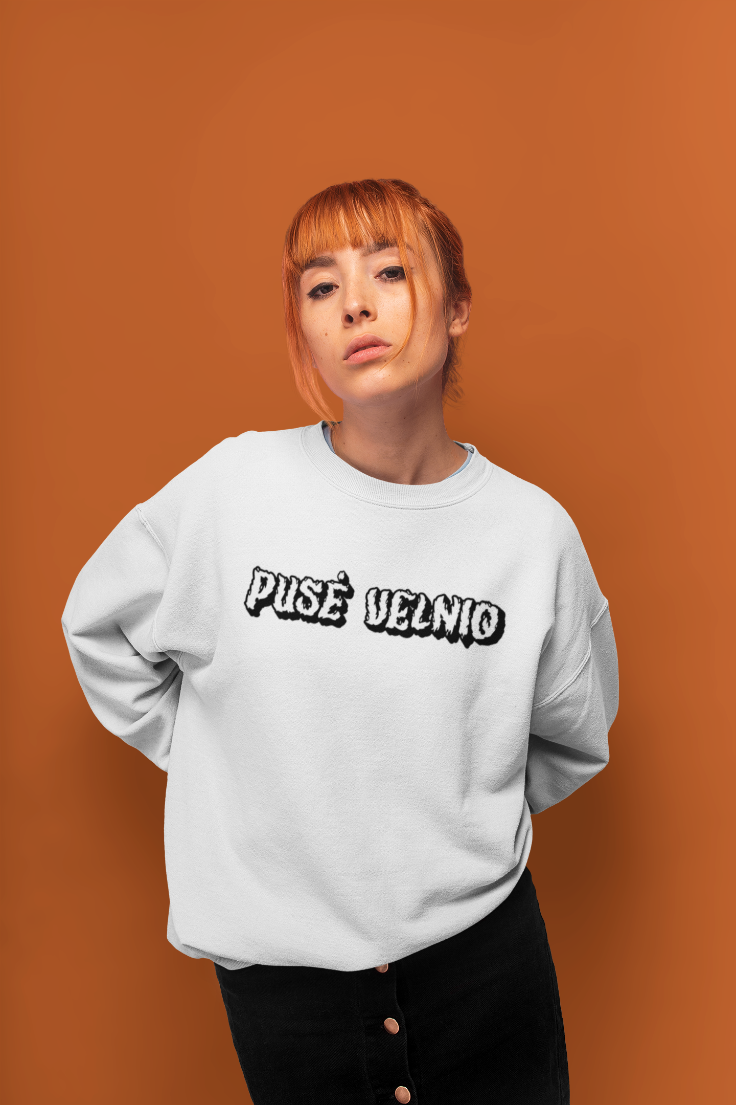 Moteris dėvi baltą džemperį su išraiškingu užrašu „Pusė velnio“ - tai drąsus, žaismingas lietuviškas dizainas.