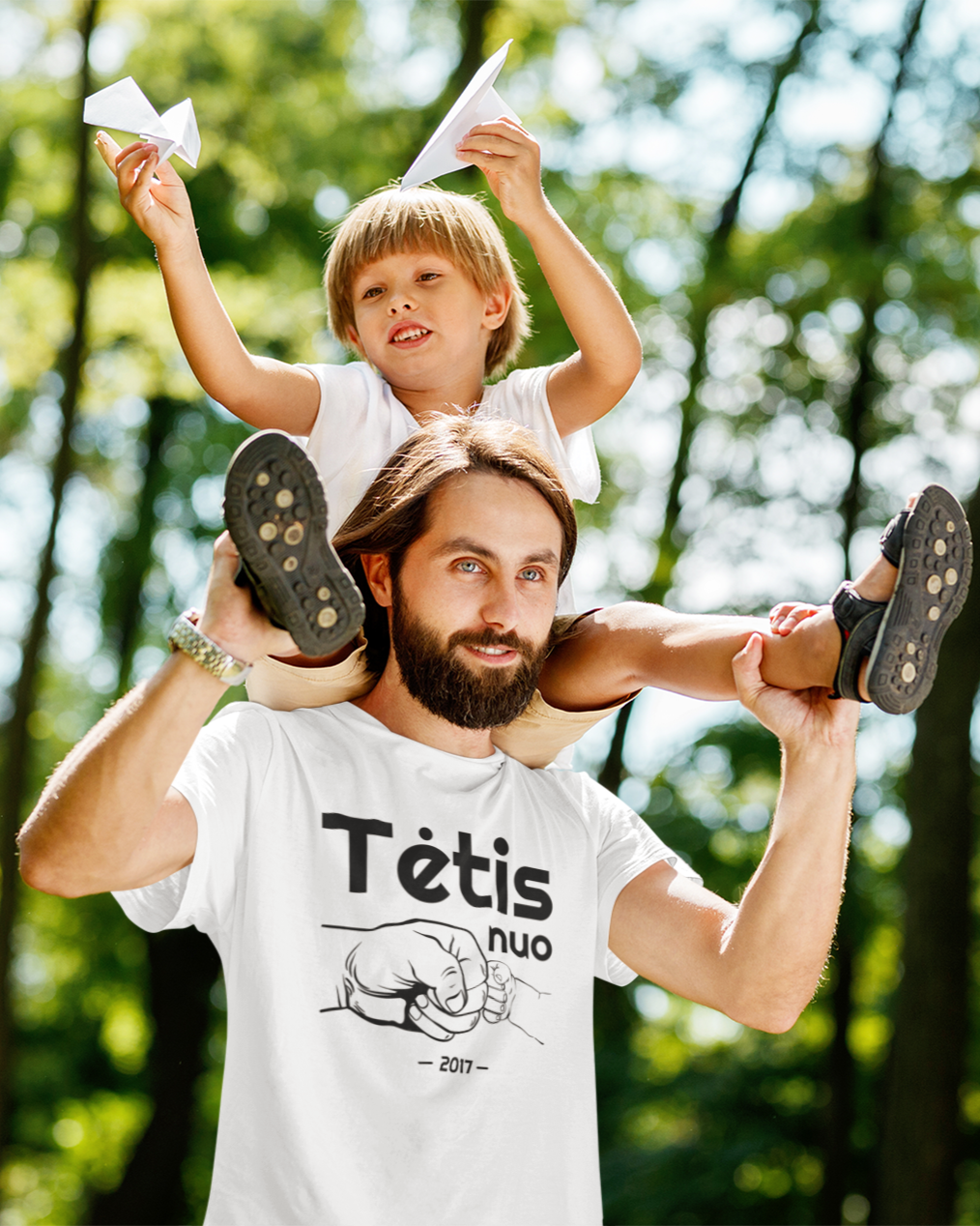 Barzdotas tėtis apsivilkęs personalizuojamais tėčio dienos marškinėliais „Tėtis nuo 2017 “ neša sūnų ant pečių parke.