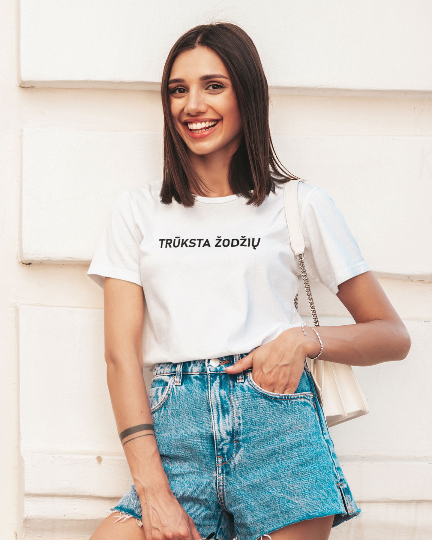 Modelis pozuoja apsirengusi džinsiniais šortais ir baltais marškinėliais su juodu užrašu "Trūksta žodžių" ant krūtinės.