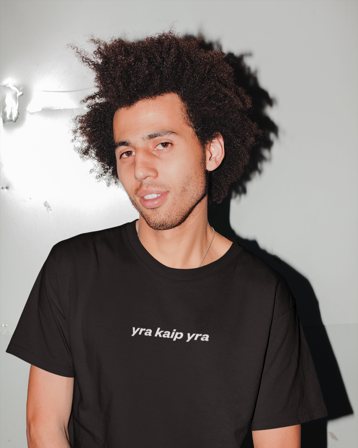 Vyras vilkintis juodus marškinėlius su užrašu „yra kaip yra“ – nuotaikingas lietuviškas dizainas su lietuviška fraze.